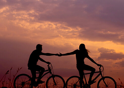 Couple holding hands and riding bicycles.